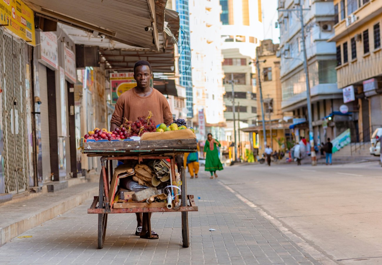A man pushing a cart of fruit down a street in Dar es Salaam